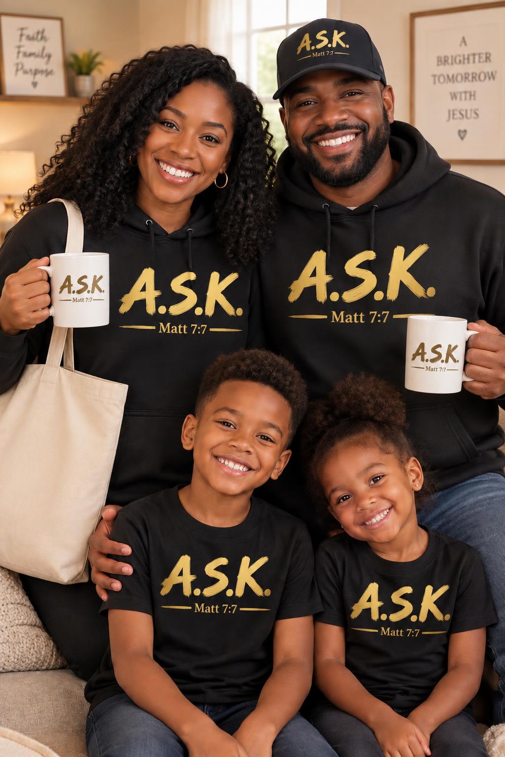 A Black family together at home, all four in the gold A.S.K. / Matt 7:7 mark — mom and dad in black A.S.K. hoodies each holding a mug printed with the mark, dad in the matching cap