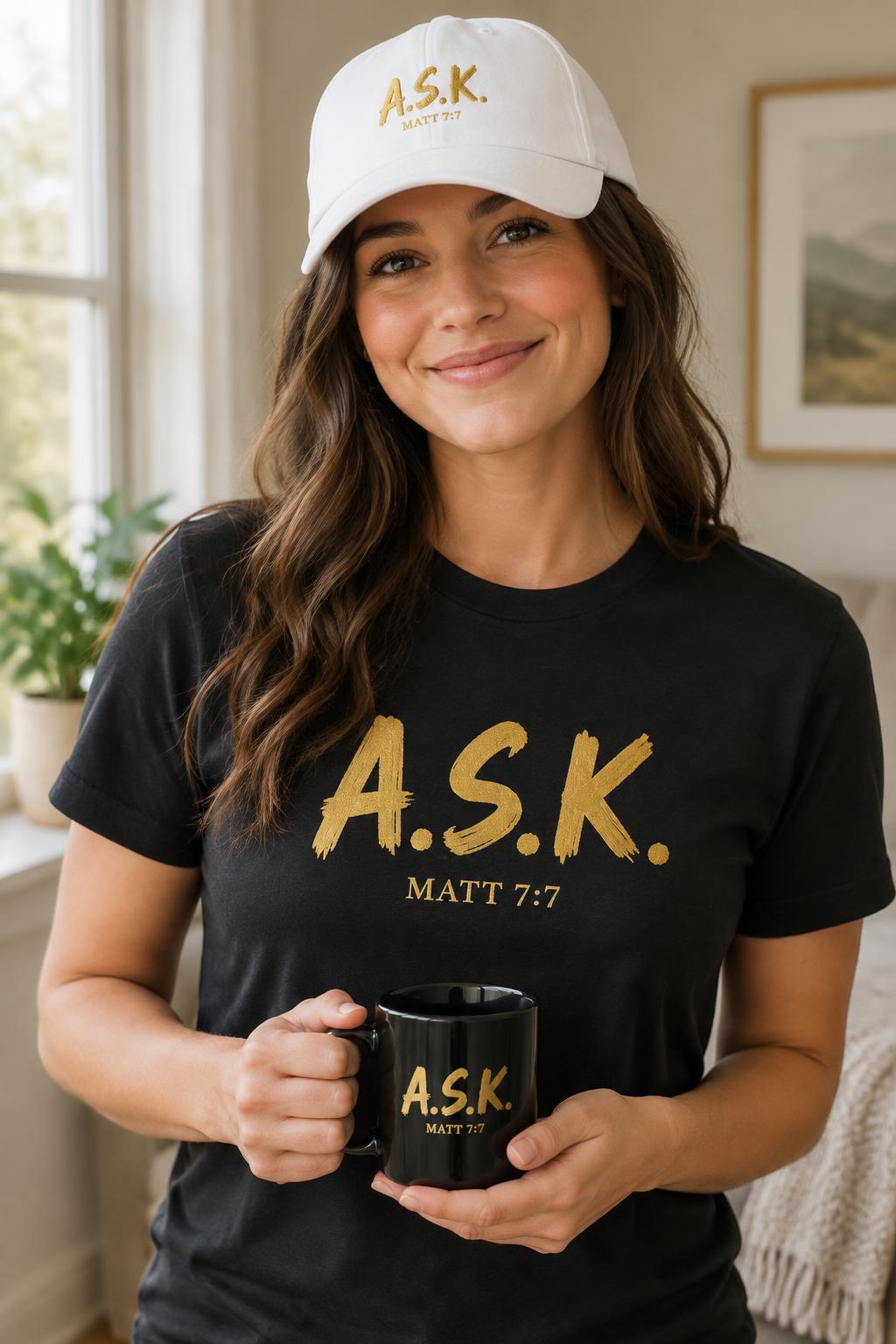 Woman smiling in a black A.S.K. tee and matching cap, holding the A.S.K. coffee mug