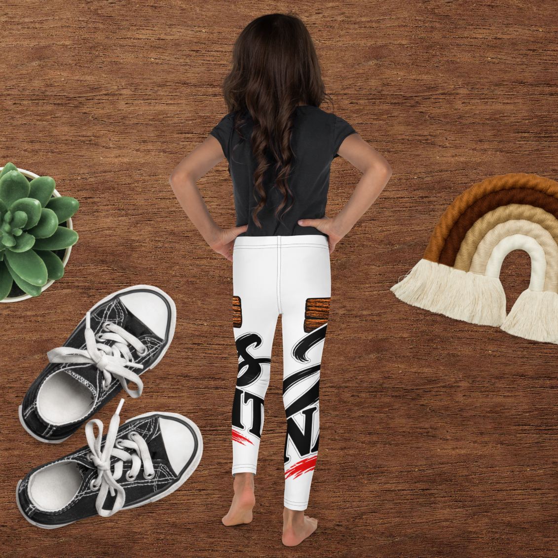 Girl from behind in a black tee and printed leggings on a wood background